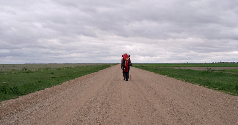 Photographic still from the film Bastards' Road of Jon Hancock walking alone down a Midwest highway