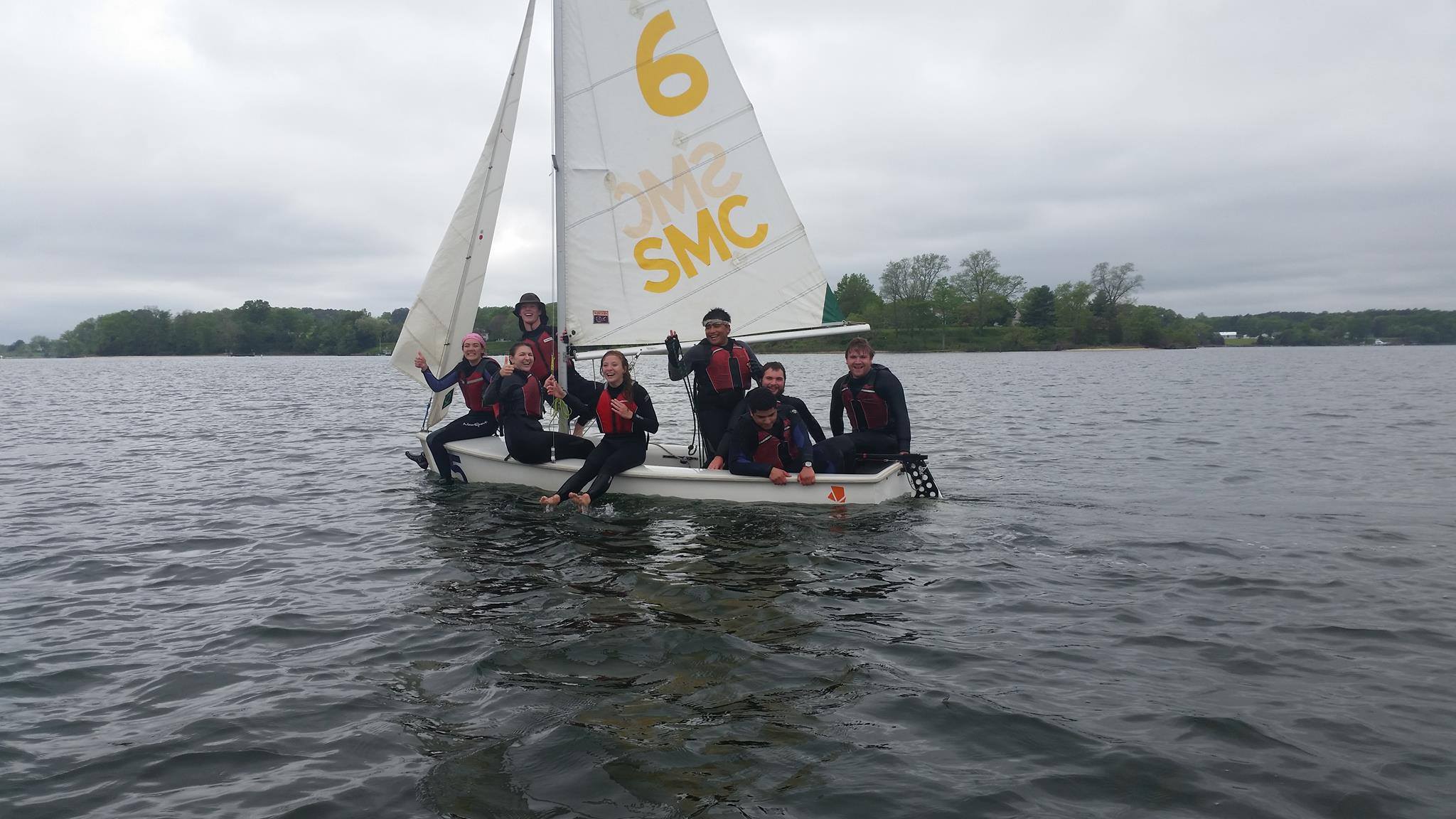A sailing team smiles from a sailboat in the middle of the river