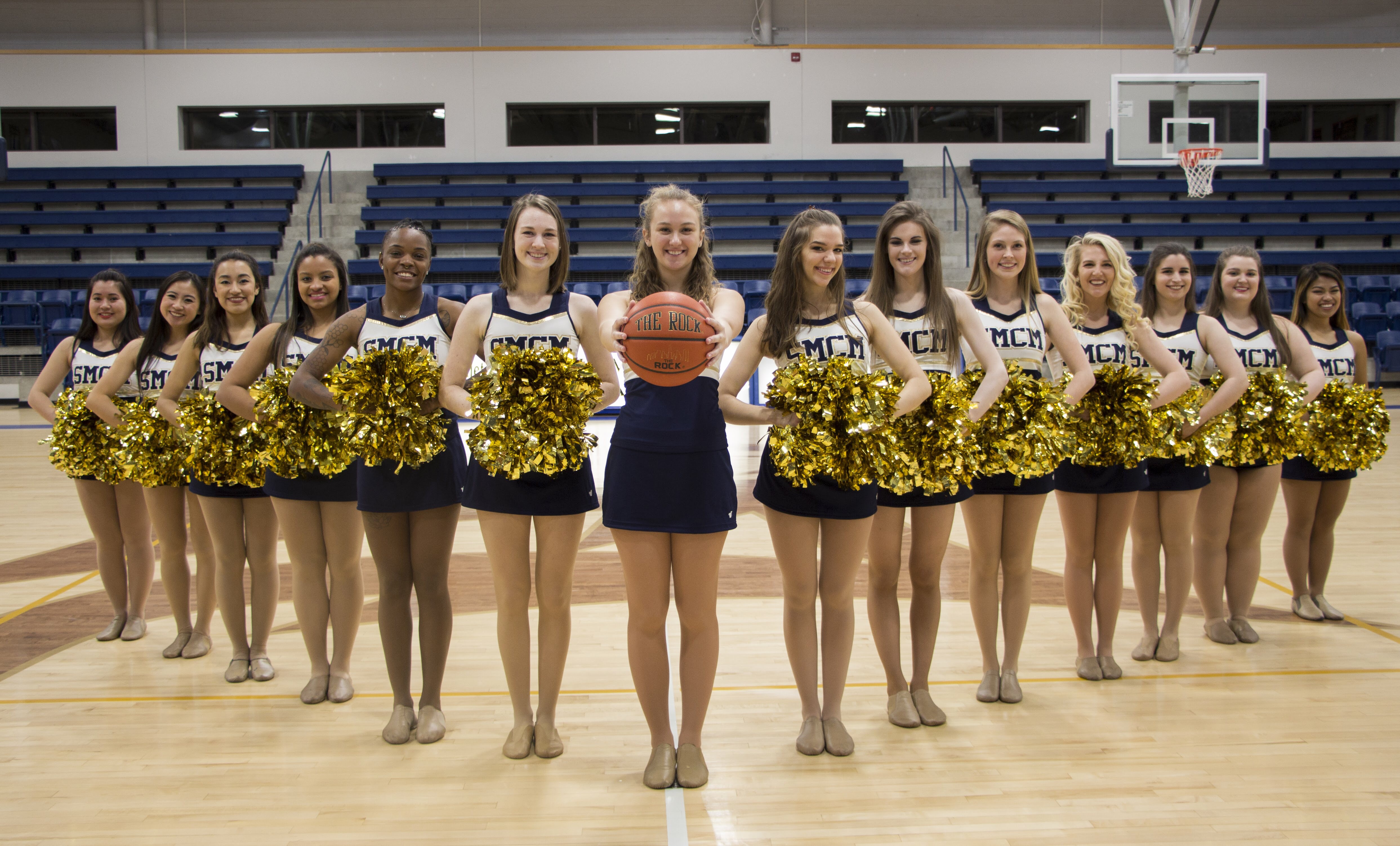 A group of cheerleaders standing in a triangle formation on an indoor basketball court.