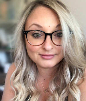 Woman with long blonde wavy hair wearing glasses.