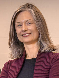 photo showing a headshot of Dr. Lipinksi, a woman with straight gray/brown hair, dressed in a black shirt and purple sweater, smiling at the camera 