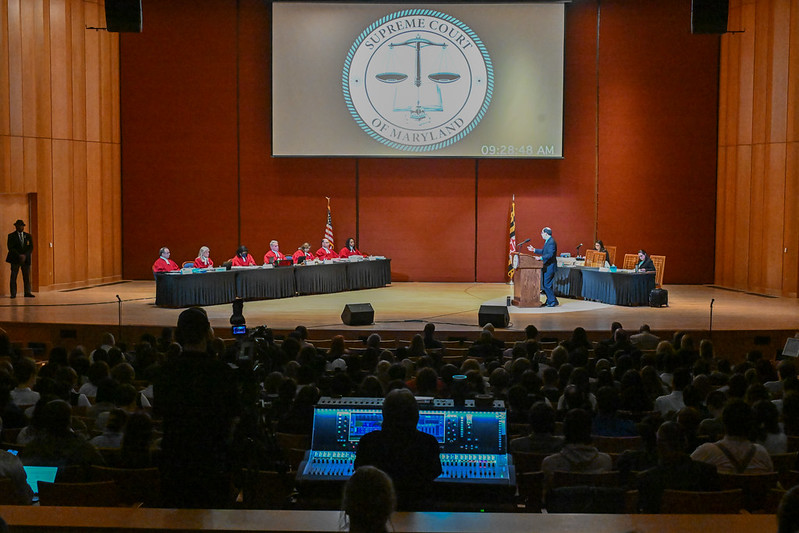 Supreme Court justices on stage hear oral arguments in front of large audience