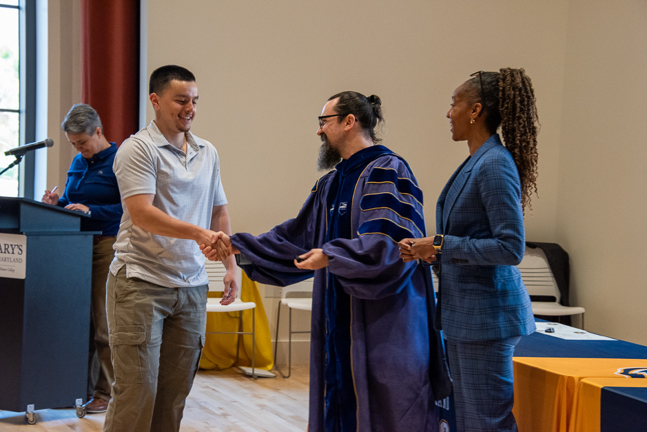 Student-Athlete Casey Cruz shakes hands with Associate Professor of Chemistry Geoffrey Bowers and Athletic Director Crystal Gibson in the recital hall of the Dodge Performing Arts Center 