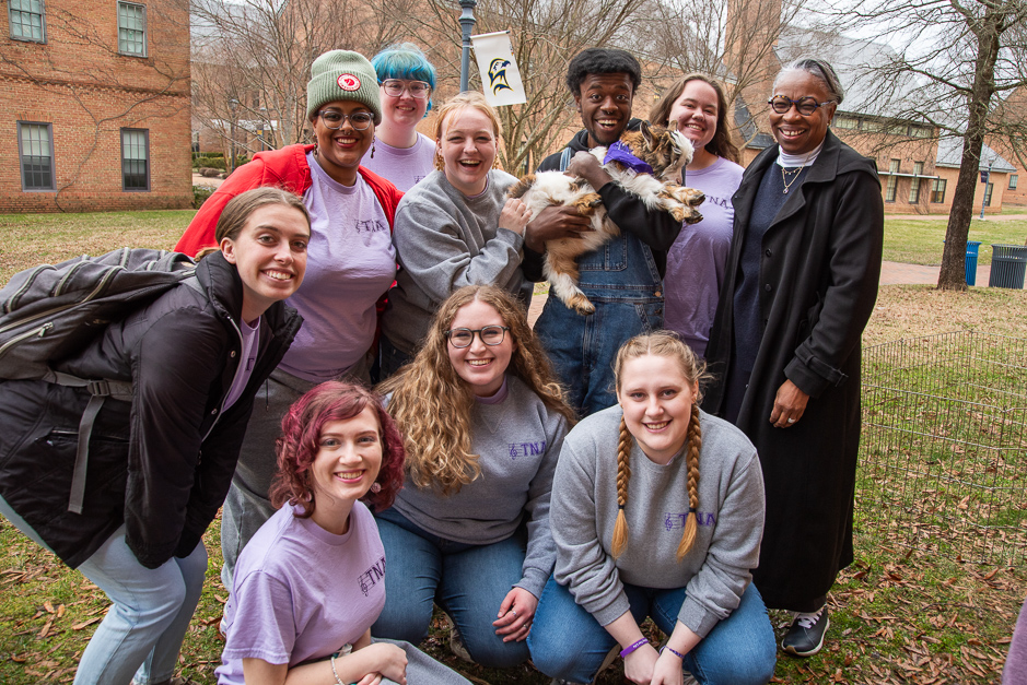 President Jordan and a group of students pose with a young goat outside on campus