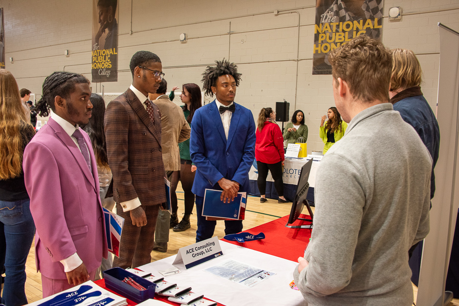 three SMCM Students stand and a booth listening to recruiters from a local consultant team  at the Spring 2024 Career and Internship Fair