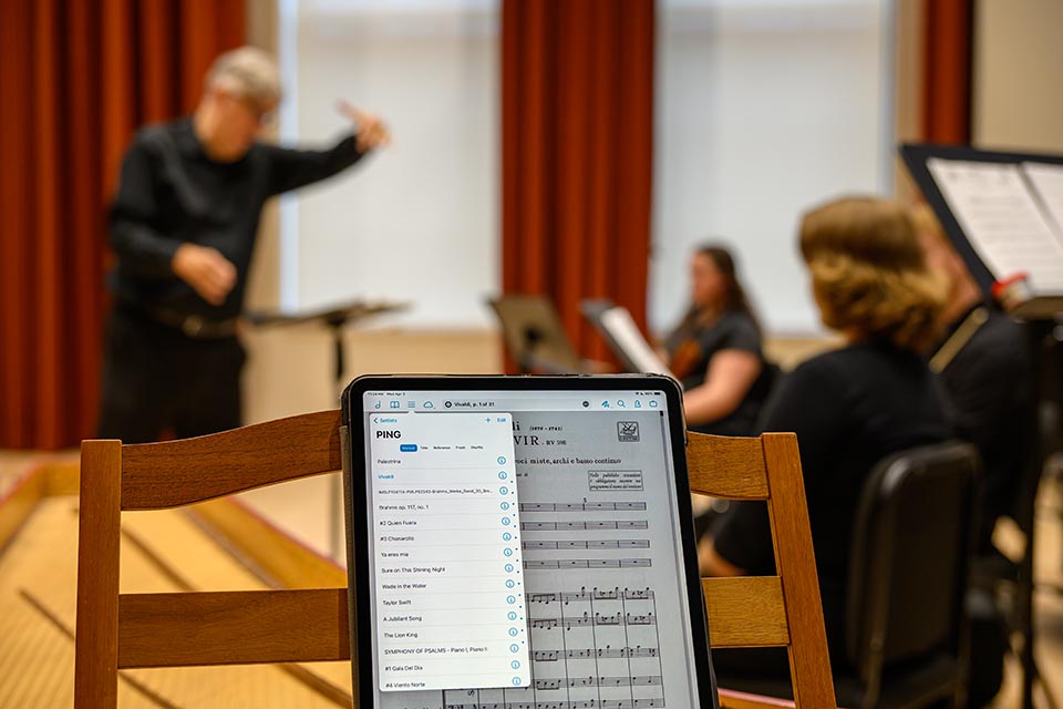 Man conducting musicians and singers with harpsichord in foreground