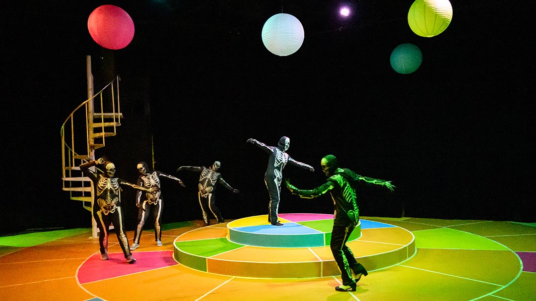 Actors dressed as skeletons dance around on colorful stage