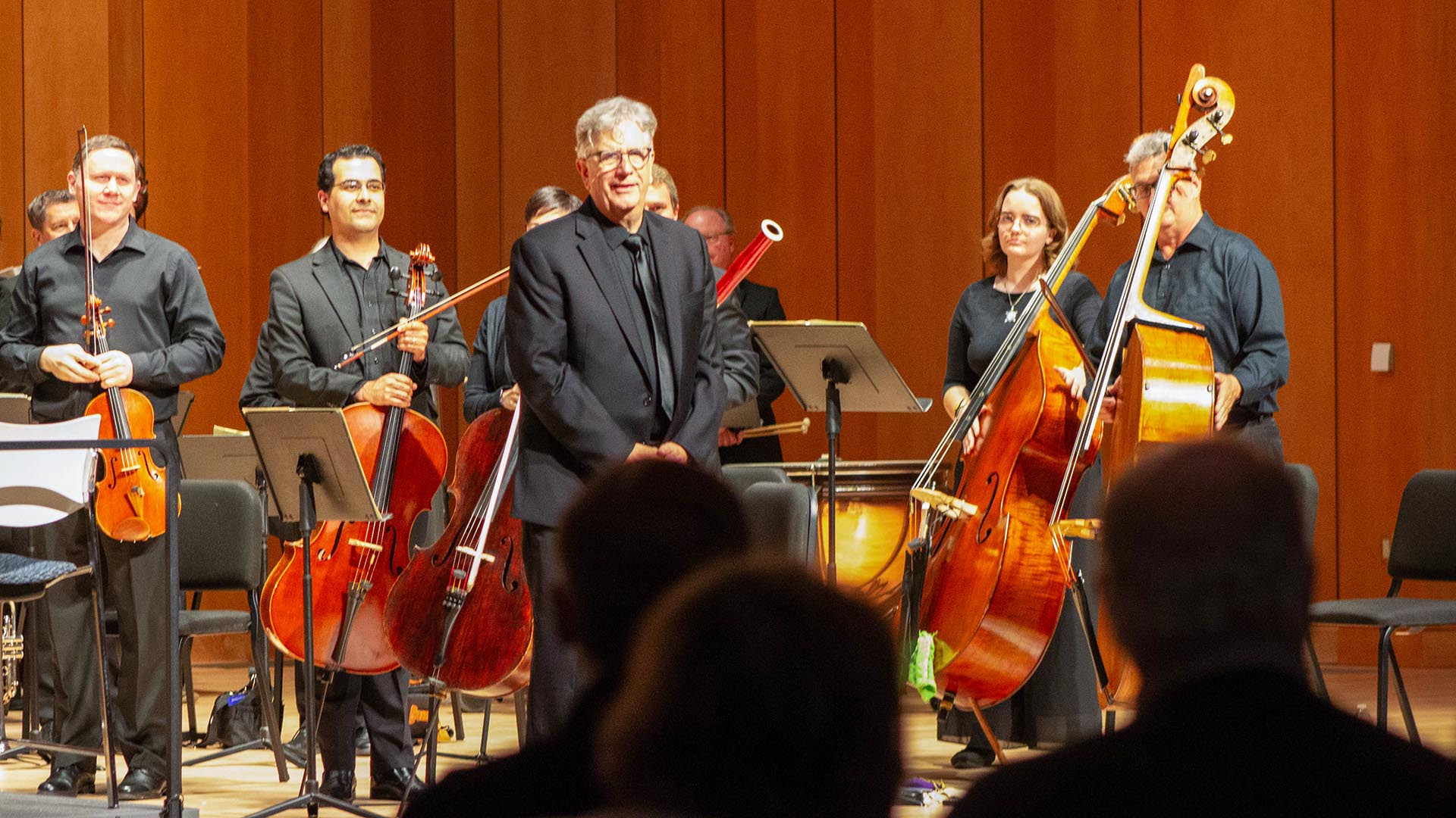 Conductor on stage in front of orchestra receiving standing ovation