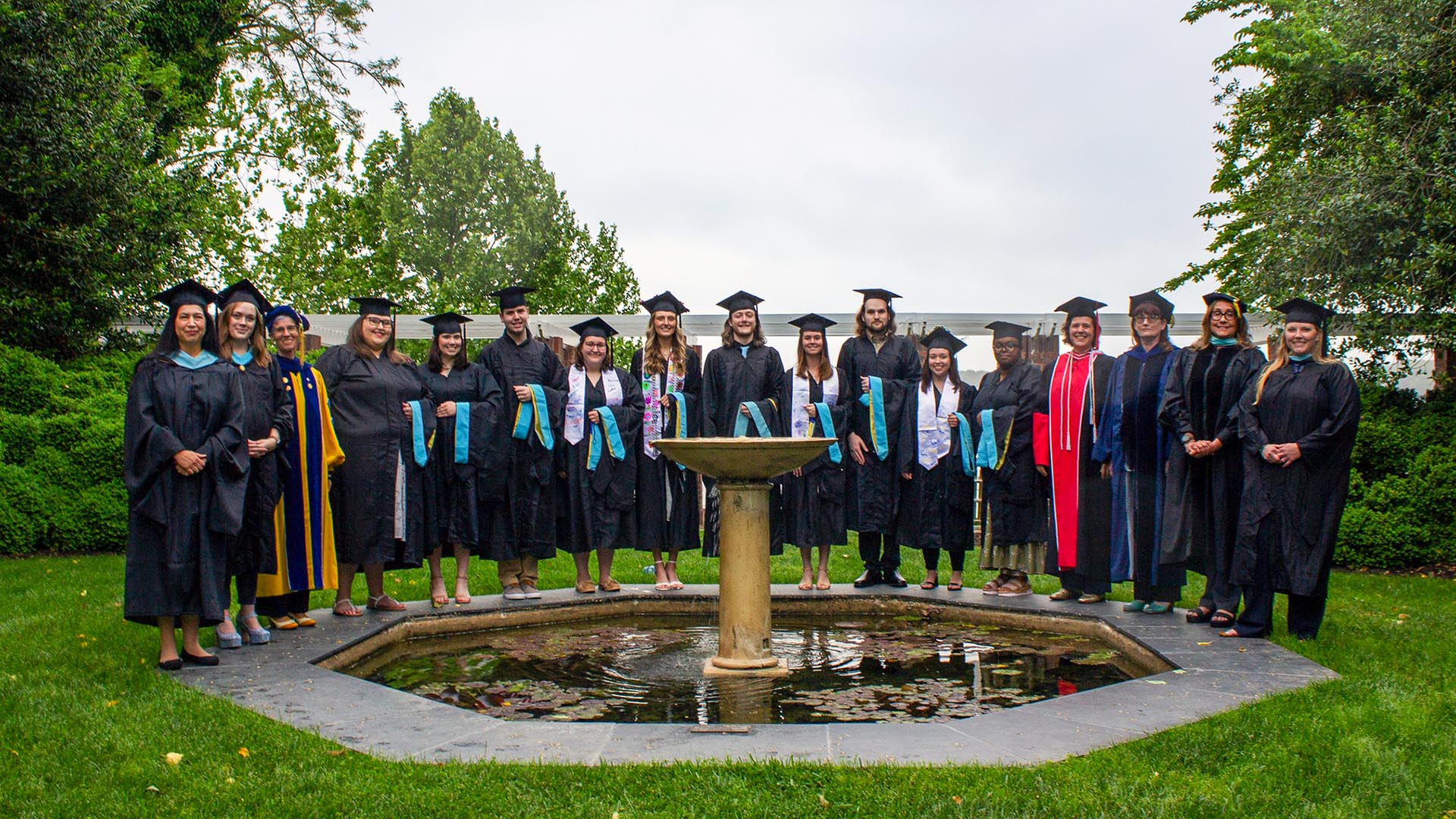 Students and faculty in caps and gowns gathered around Remembrance Garden 