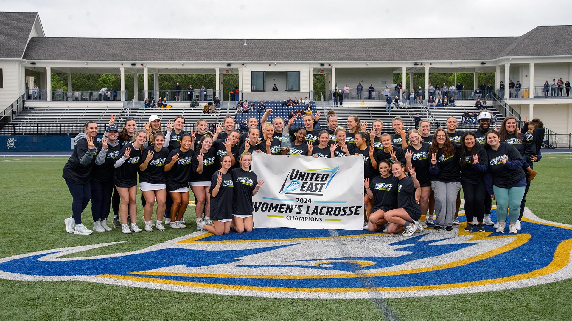 Women's lacrosse team and caches with championship banner