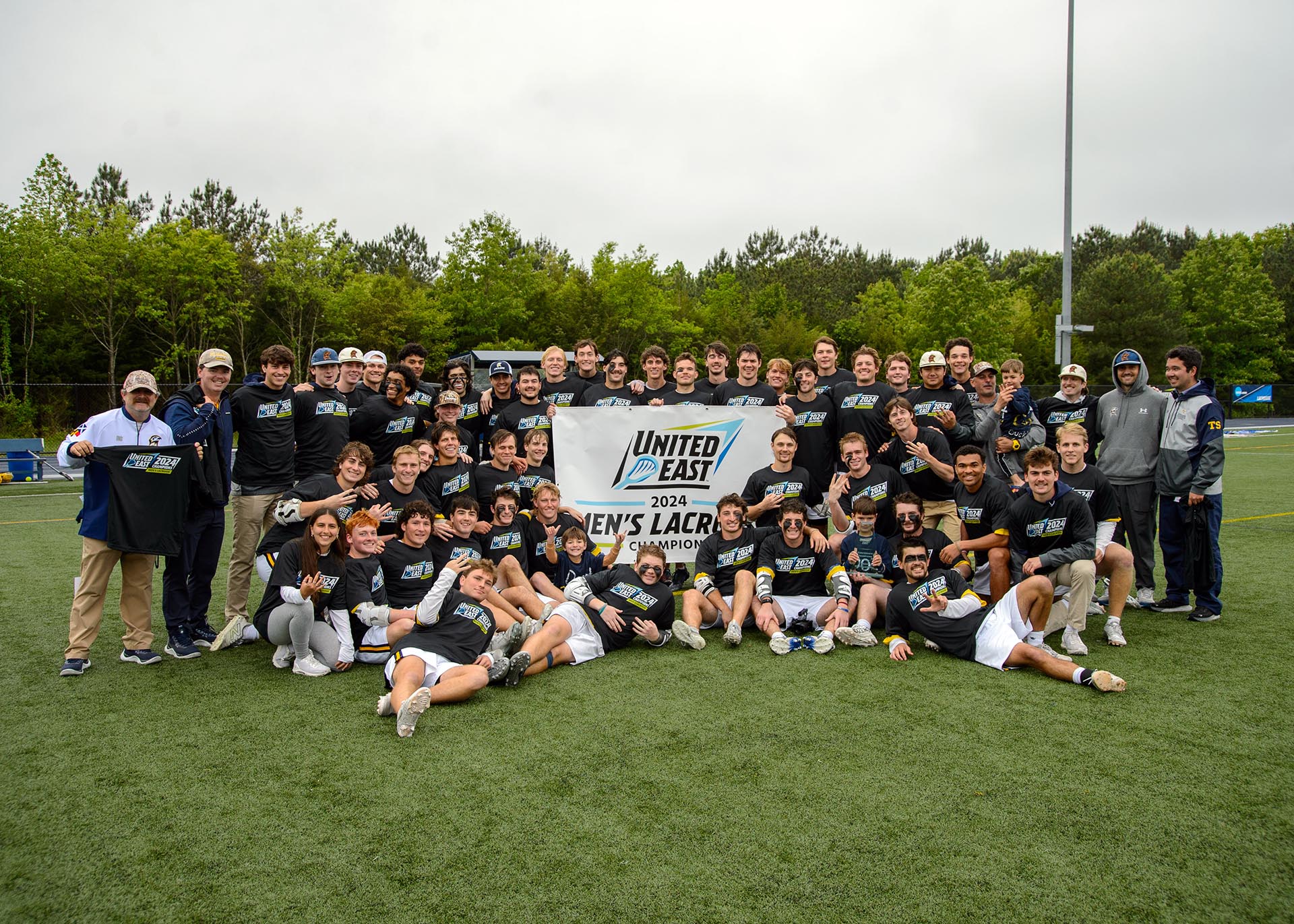 Lacrosse team and coaches with United East championship banner