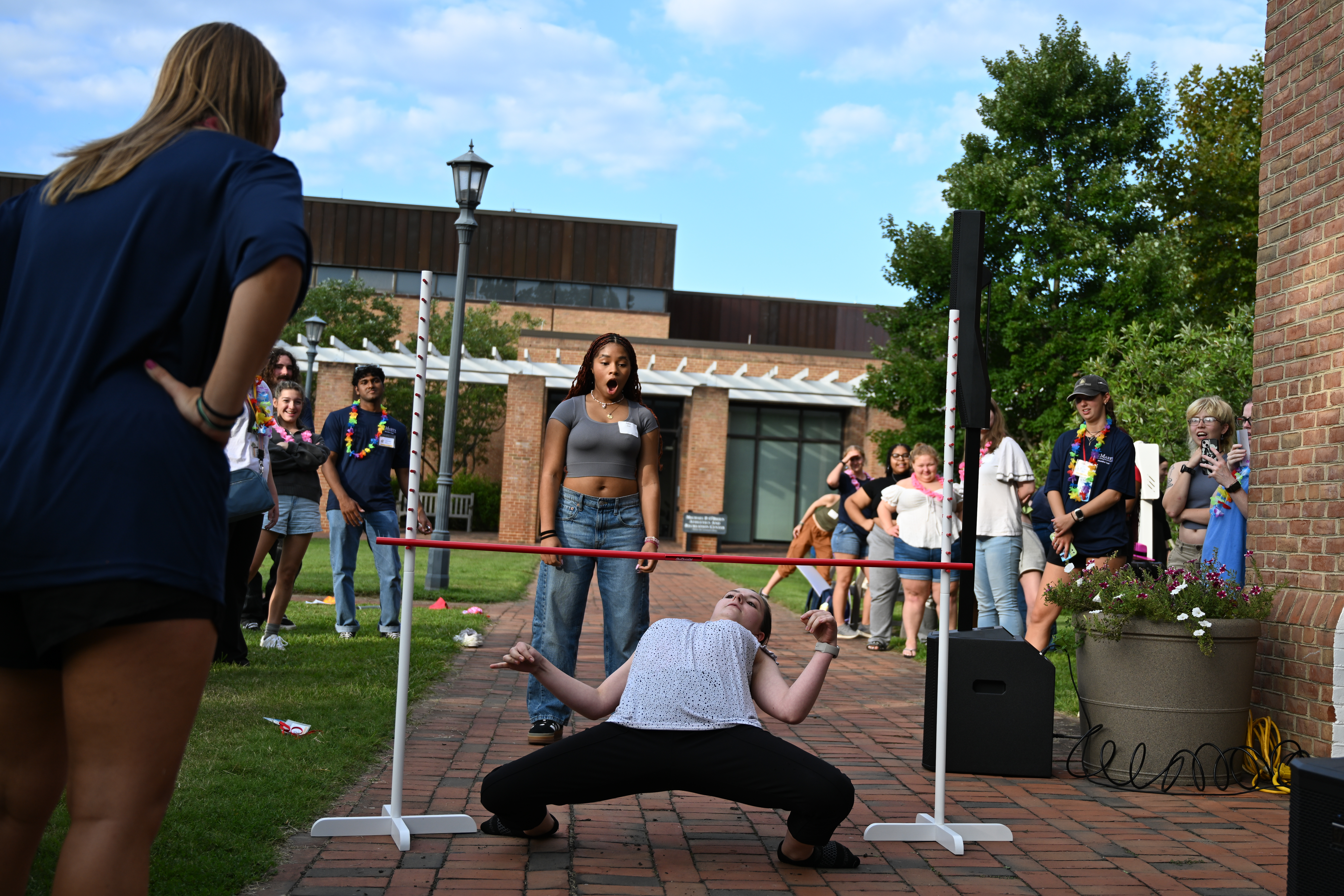 A young woman attempts to limbo under a stick while a crowd observes 