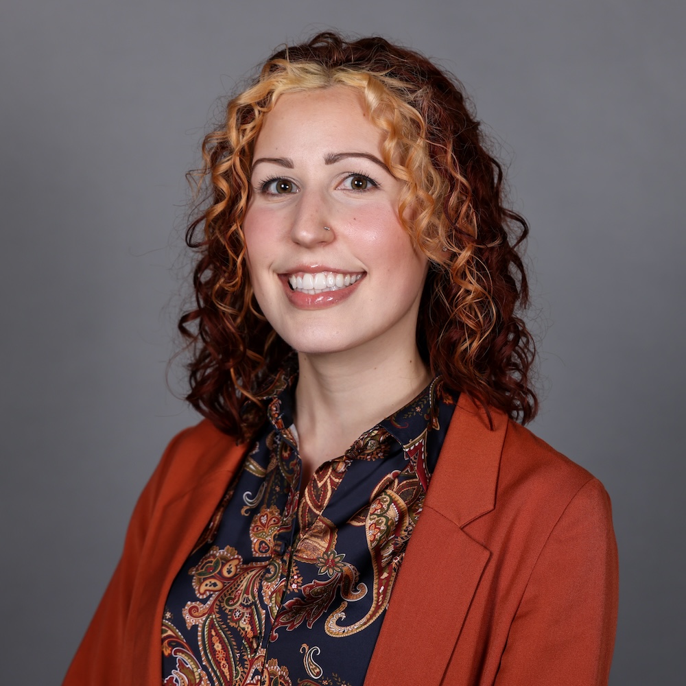 Woman smiling in photo with medium length brown and blond curly hair.