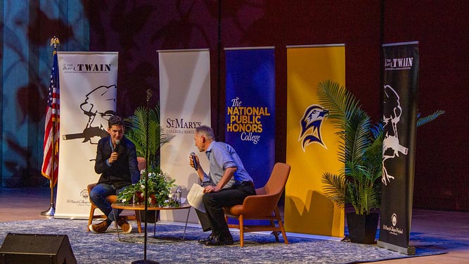 Two men seated on stage talking