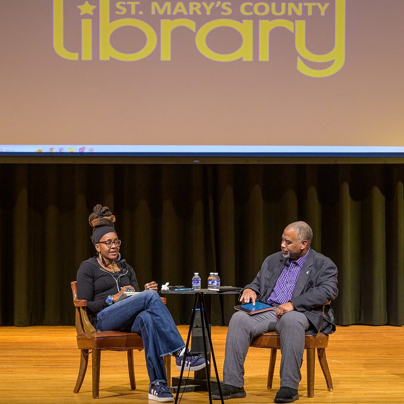 Woman and man seated on stage in front of words "St. Mary's County Library" projectedon screen