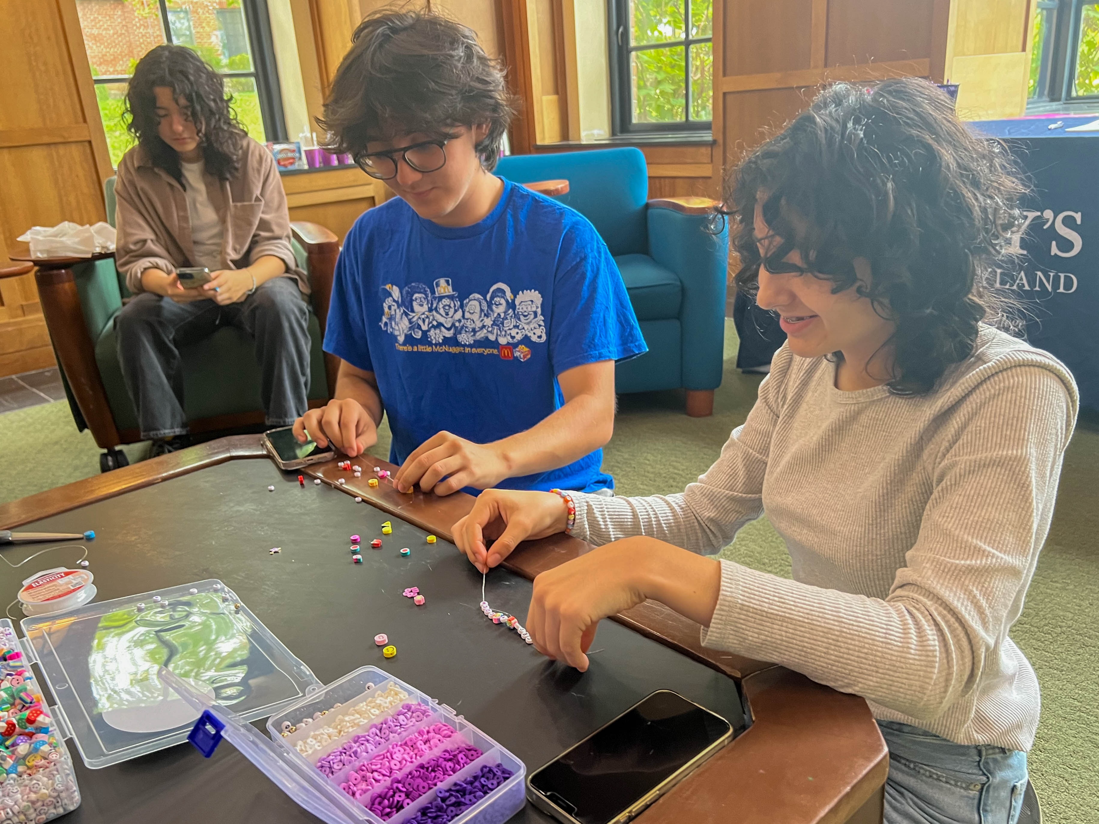 Two students craft friendship bracelets at a table 