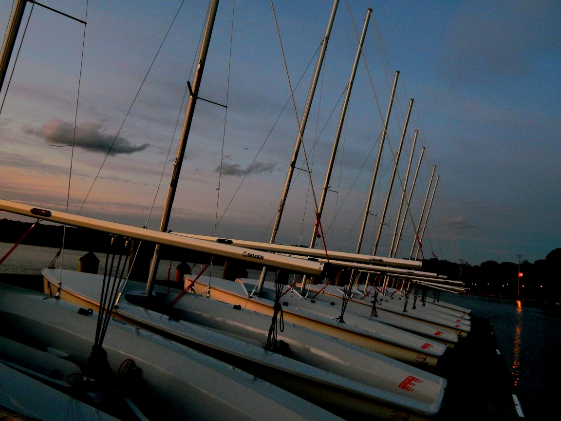 Sailboats lined up by the dock as the sun begins to set.