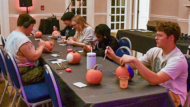 Several students seated at table decorating pumpkins