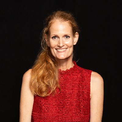 Dr. Crystal Hoyt, person presenting female with long red hair, wearing a red sleeveless shirt against a black background