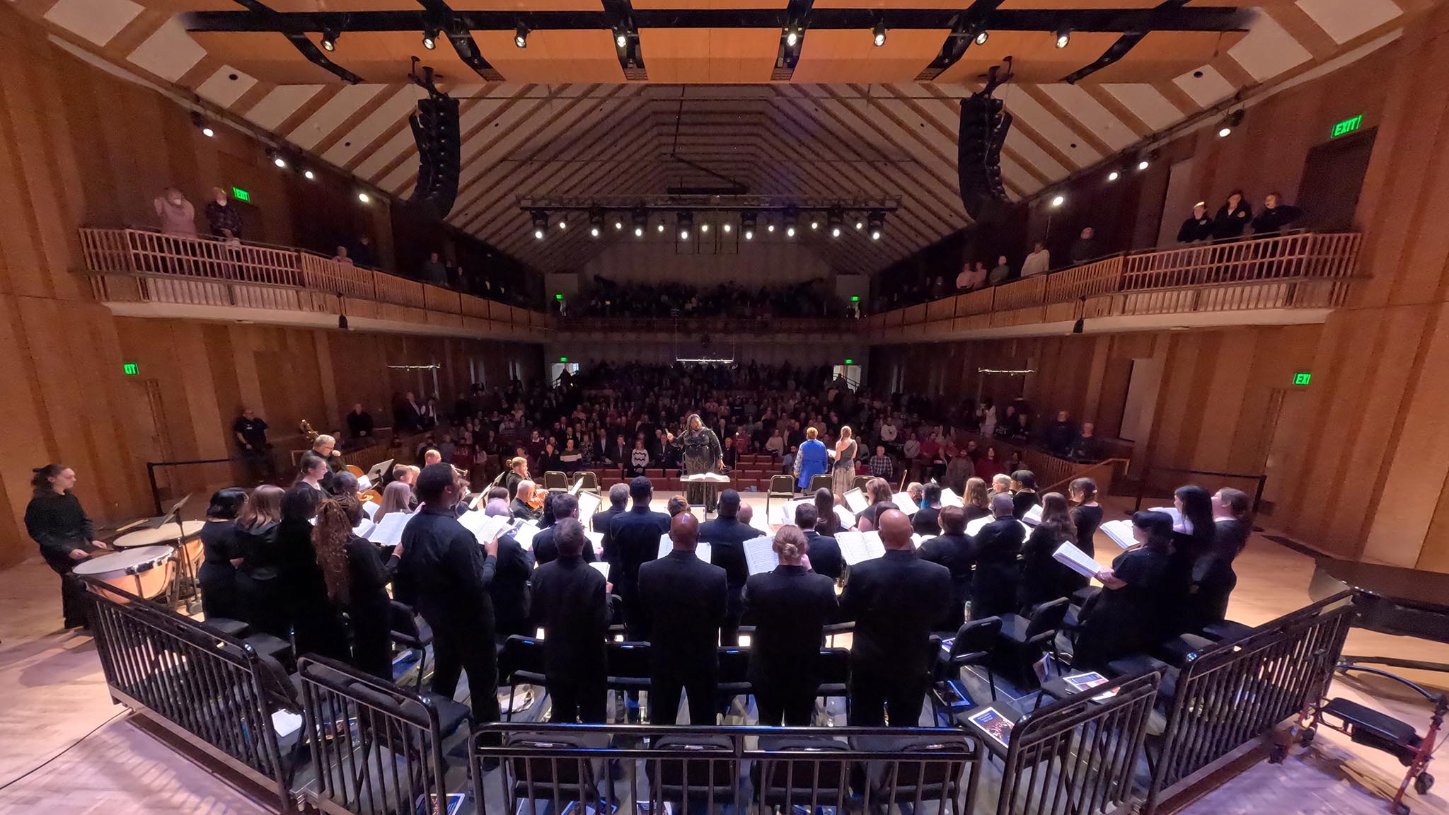 View from back of stage showing chorus and orchestra perform before packed concert hall