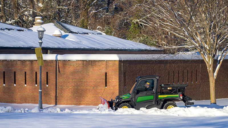 Two men in a "gator" clear snow in front of Montgomery Hall