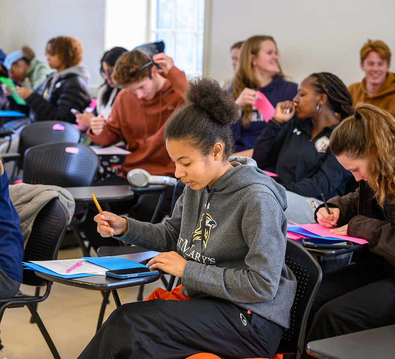 Students seated at desks writing cards