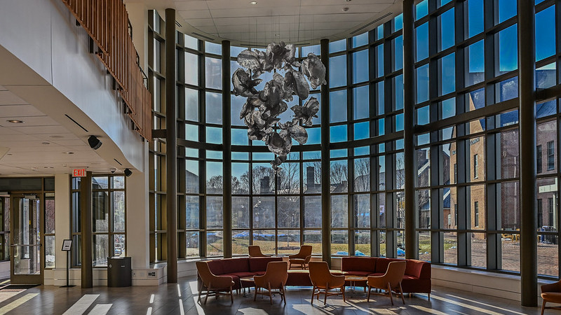 A spacious lobby featuring large windows and comfortable chairs, inviting natural light and providing a welcoming atmosphere. Oysters sculpture suspended from the ciling.