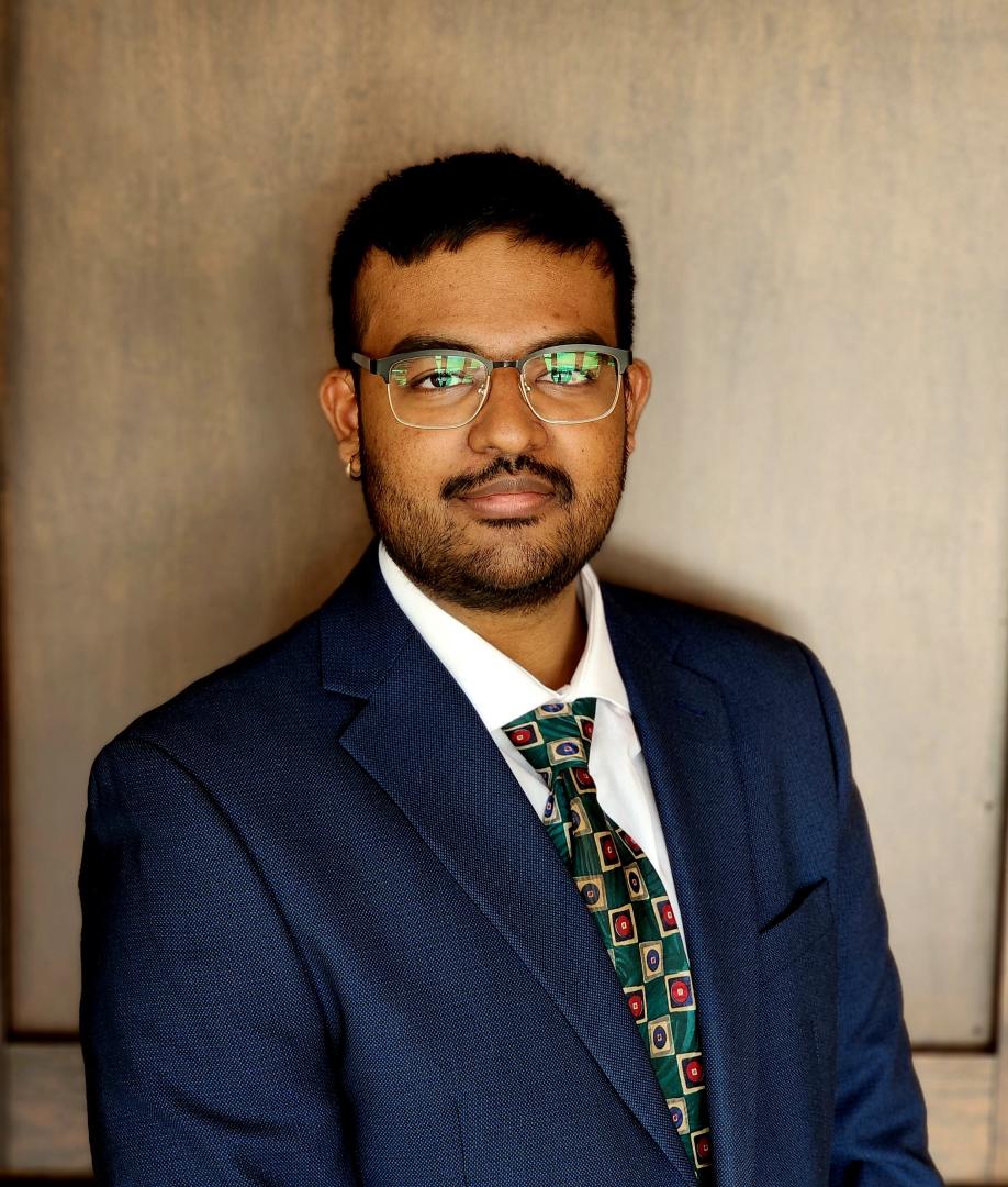 photo showing a headshot of Dr. Beharie, a man with short dark hair, glasses, and a suit and tie, looking at the camera