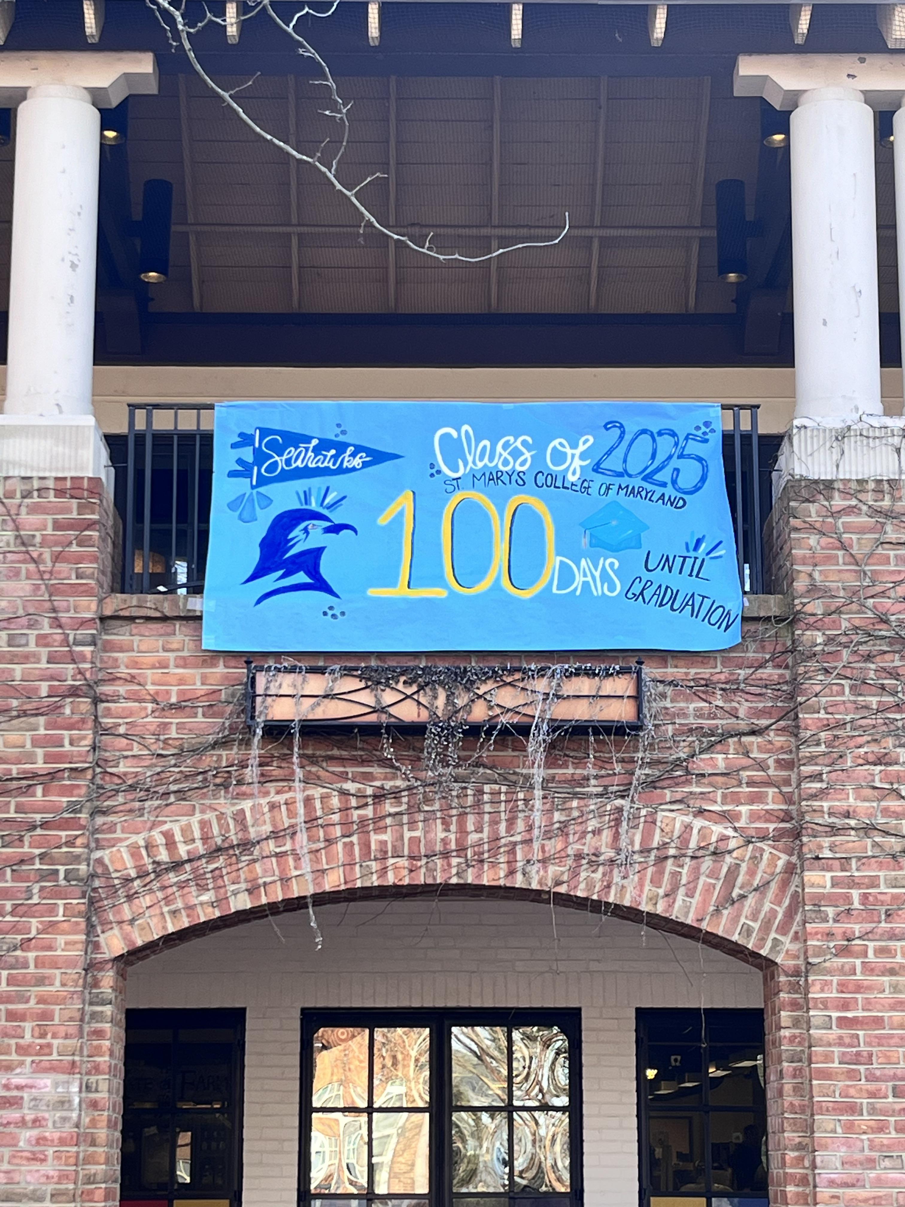 A brick building with a blue and yellow banner hanging on the balcony. The banner reads, "Class of 2025" with "100 Days Until Graduation" underneath, and "Seahawks" with a bird logo on the left.