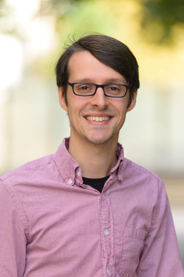 photo showing a headshot of Patrick Piantadosi, a man with brown hair, dressed in a red and white checked shirt, with black glasses, smiling at the camera 