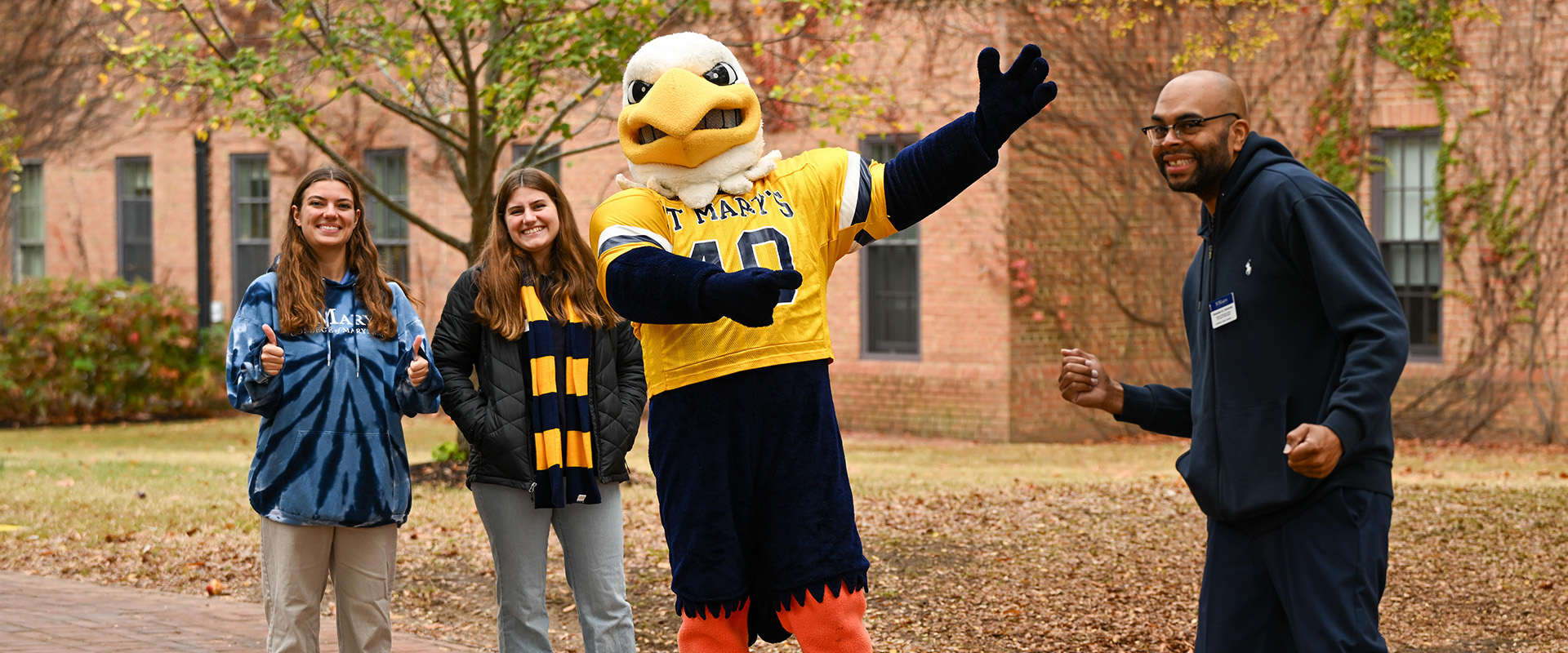 A mascot dressed as an eagle poses with two smiling women and a man outdoors. 