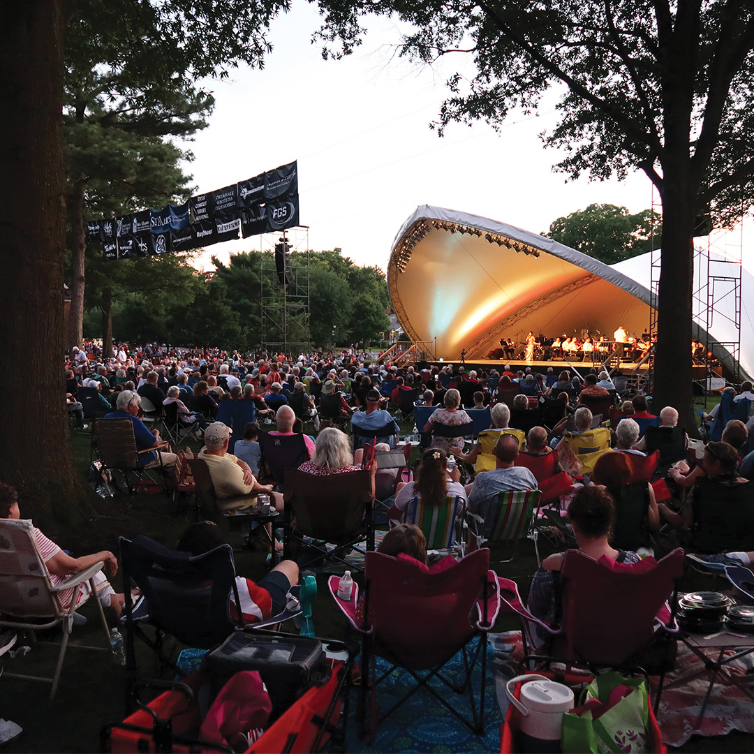 A large audience sits on lawn chairs and blankets at River Concert Series