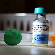A vial labeled "Measles, Mumps, Rubella Virus Vaccine" sits next to a syringe and a green cap marked "MMR.