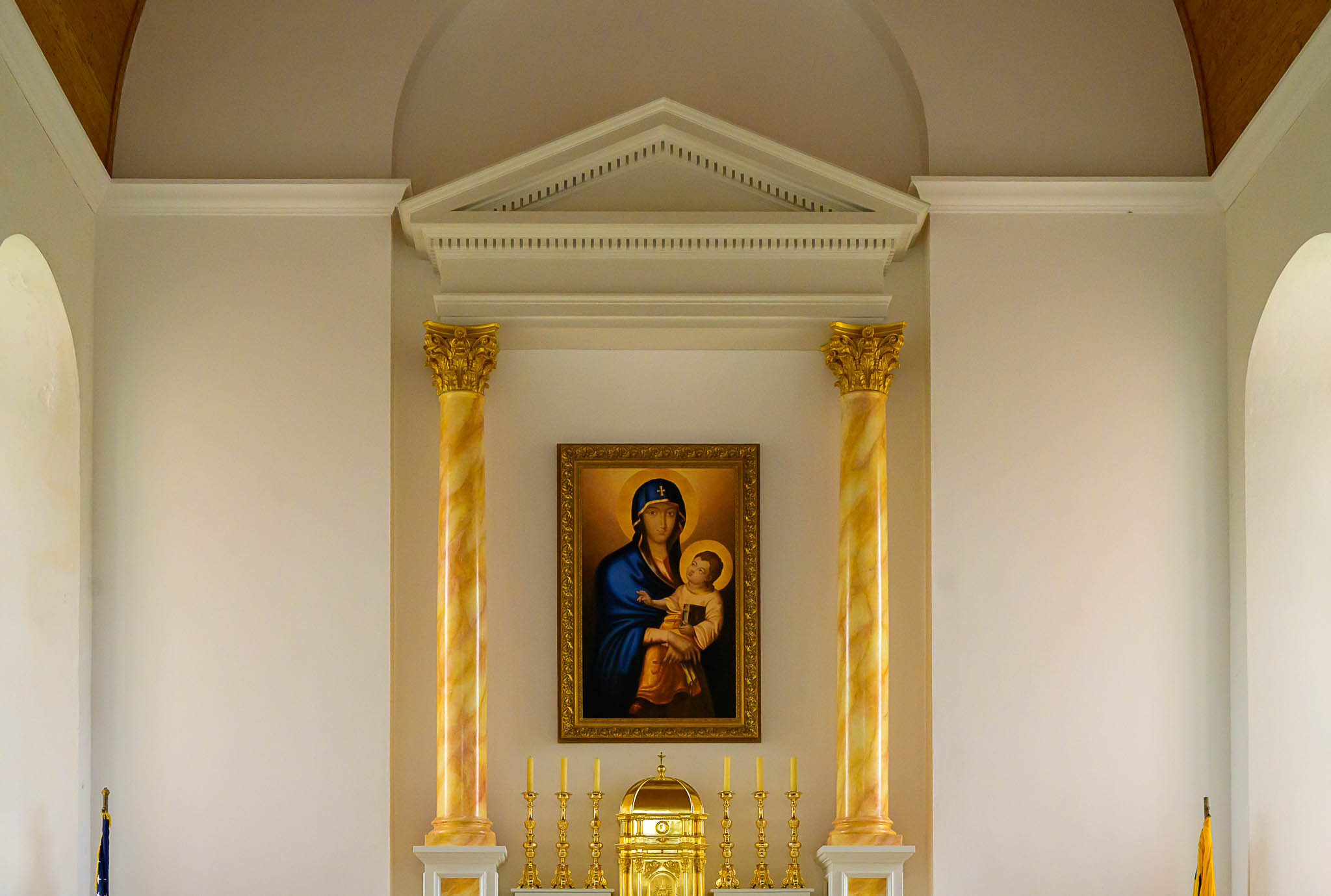 A framed painting of Madonna and Child hangs between two gold columns above a gold tabernacle and candlesticks in a church interior.