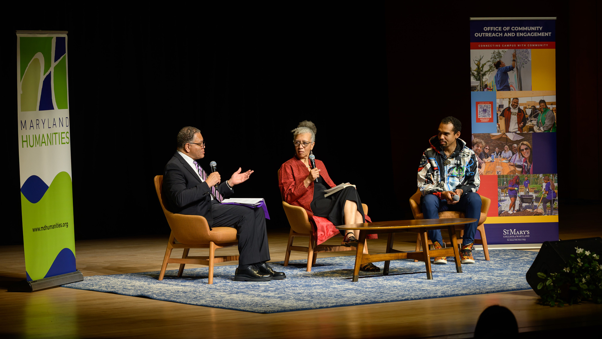 Three people sit on stage in chairs having a panel discussion, with Maryland Humanities and outreach banners in the background.
