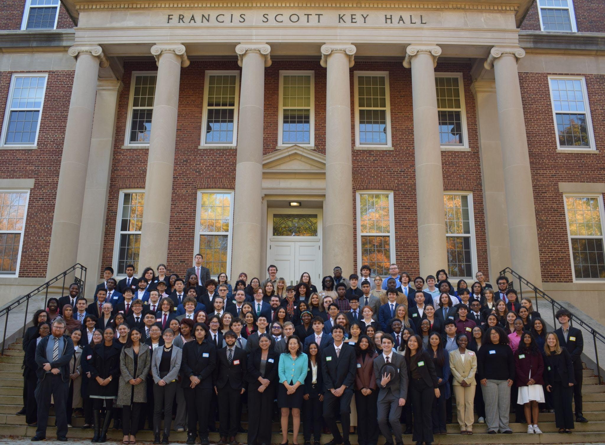 A large group of people in business attire pose for a photo on the steps of Francis Scott Key Hall, a brick building with columns.