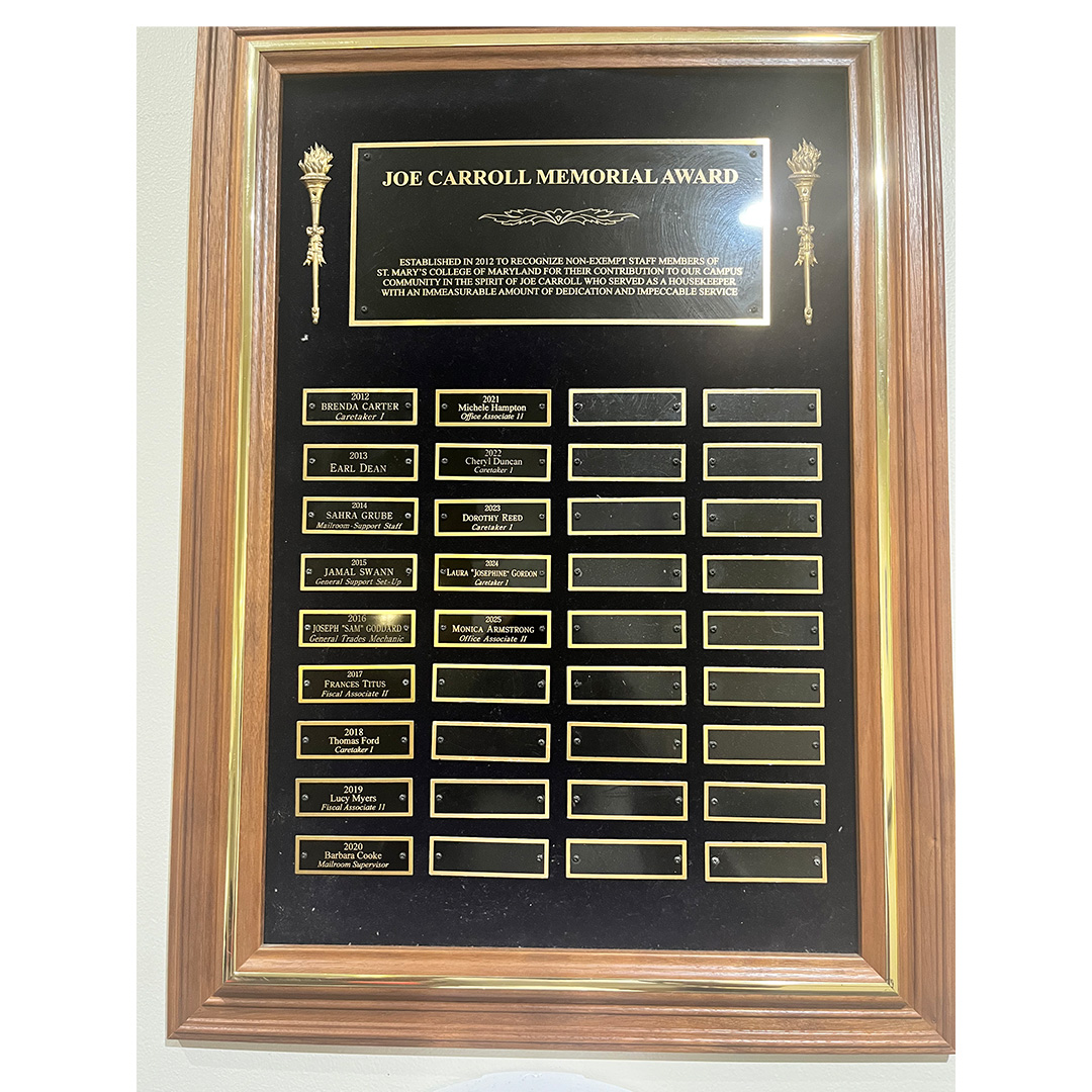 A wooden plaque titled "Joe Carroll Memorial Award" displays engraved nameplates in several rows, with some blank spaces.
