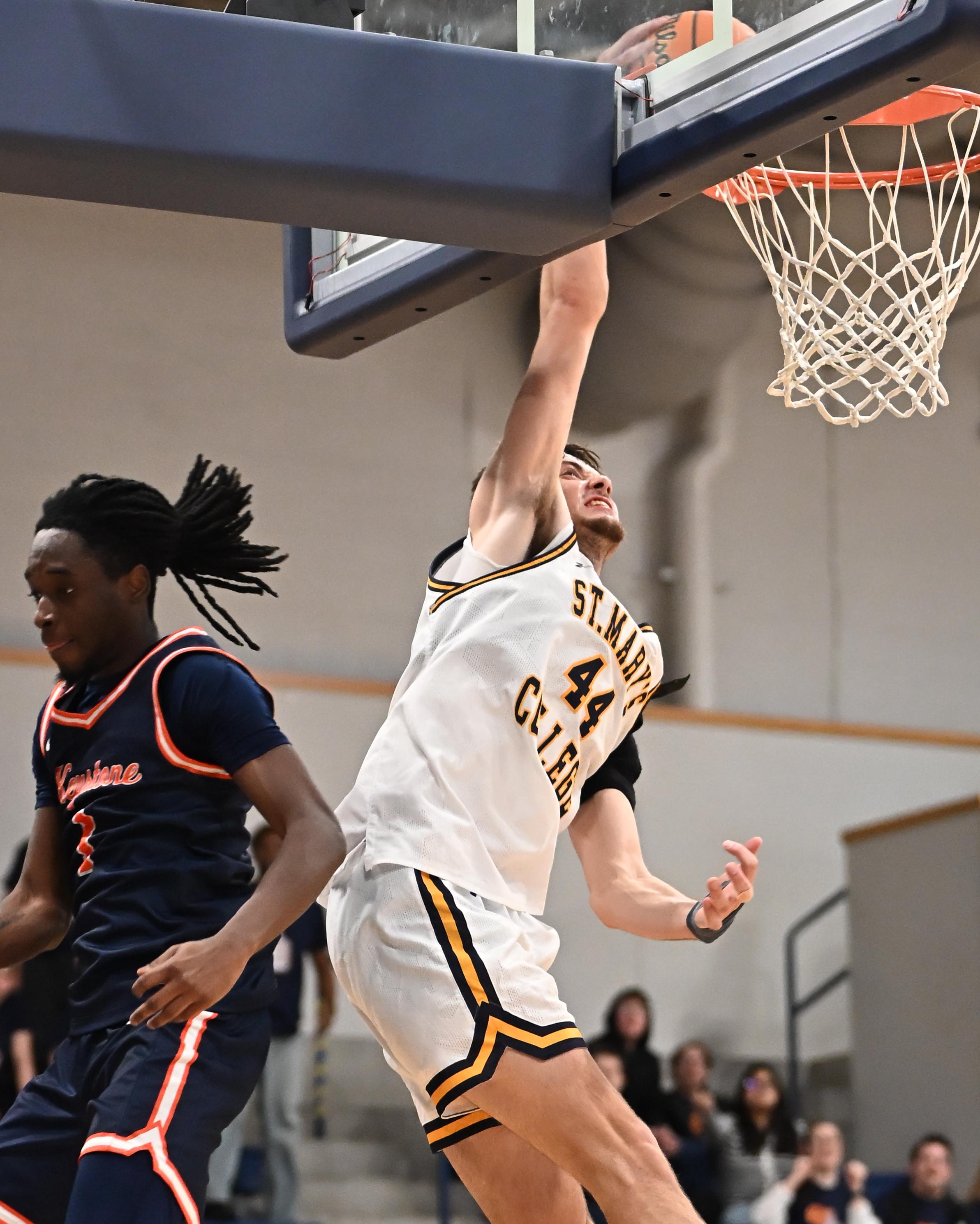 A basketball player in a white uniform attempts a layup while a defender in a dark uniform tries to block during a game.