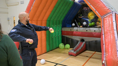 A man in uniform throws a yellow ball at an inflatable arcade game with colorful panels and scattered balls inside a gymnasium.