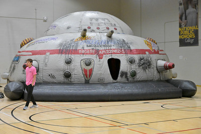 A person walks past a large inflatable spaceship structure set up inside a gymnasium.