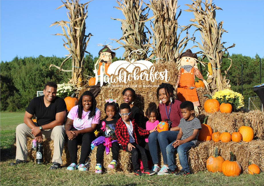 Family sitting on hay bales with fall themed decorations around them