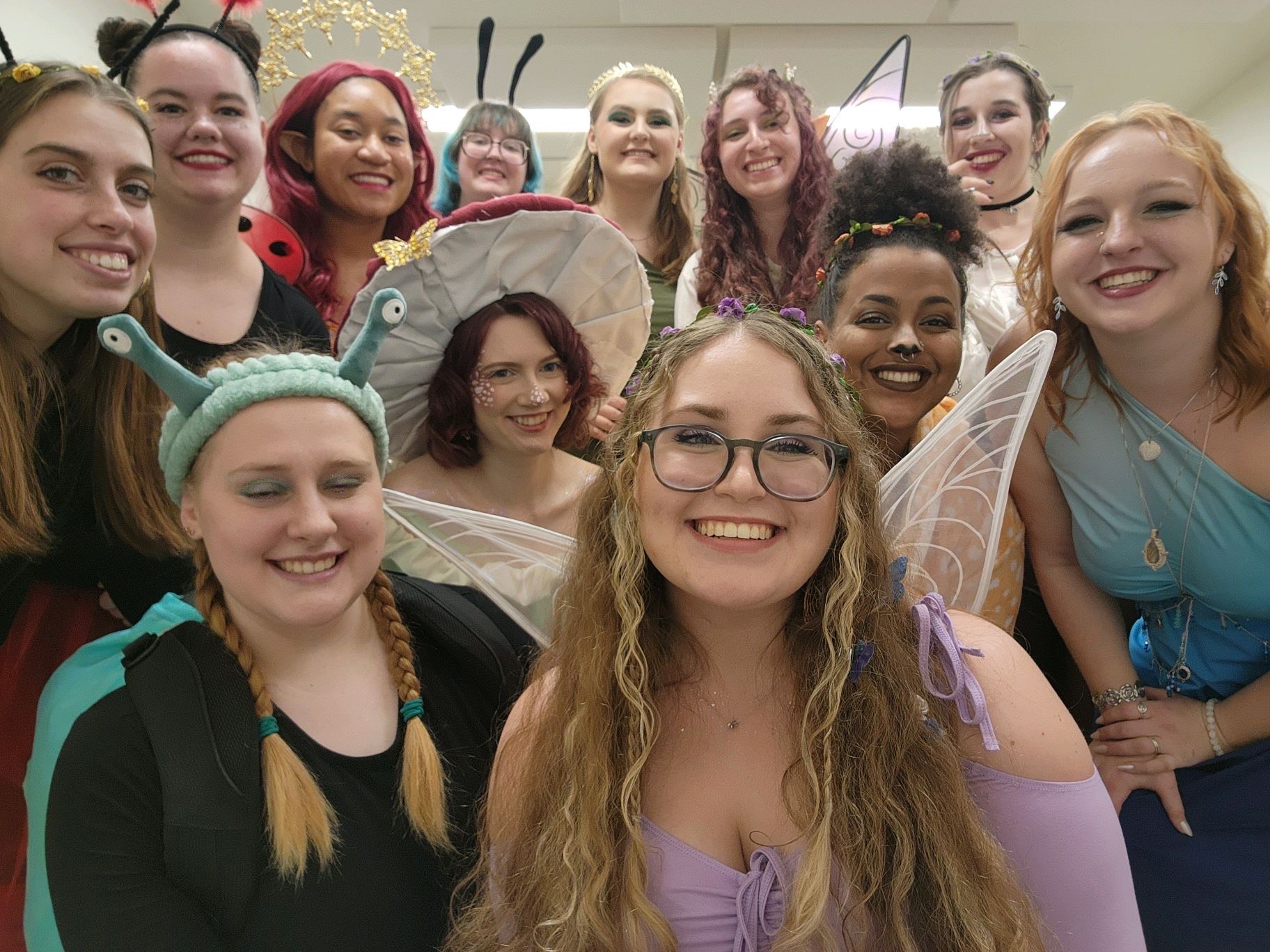 A group of people dressed in colorful, whimsical costumes pose and smile together indoors.