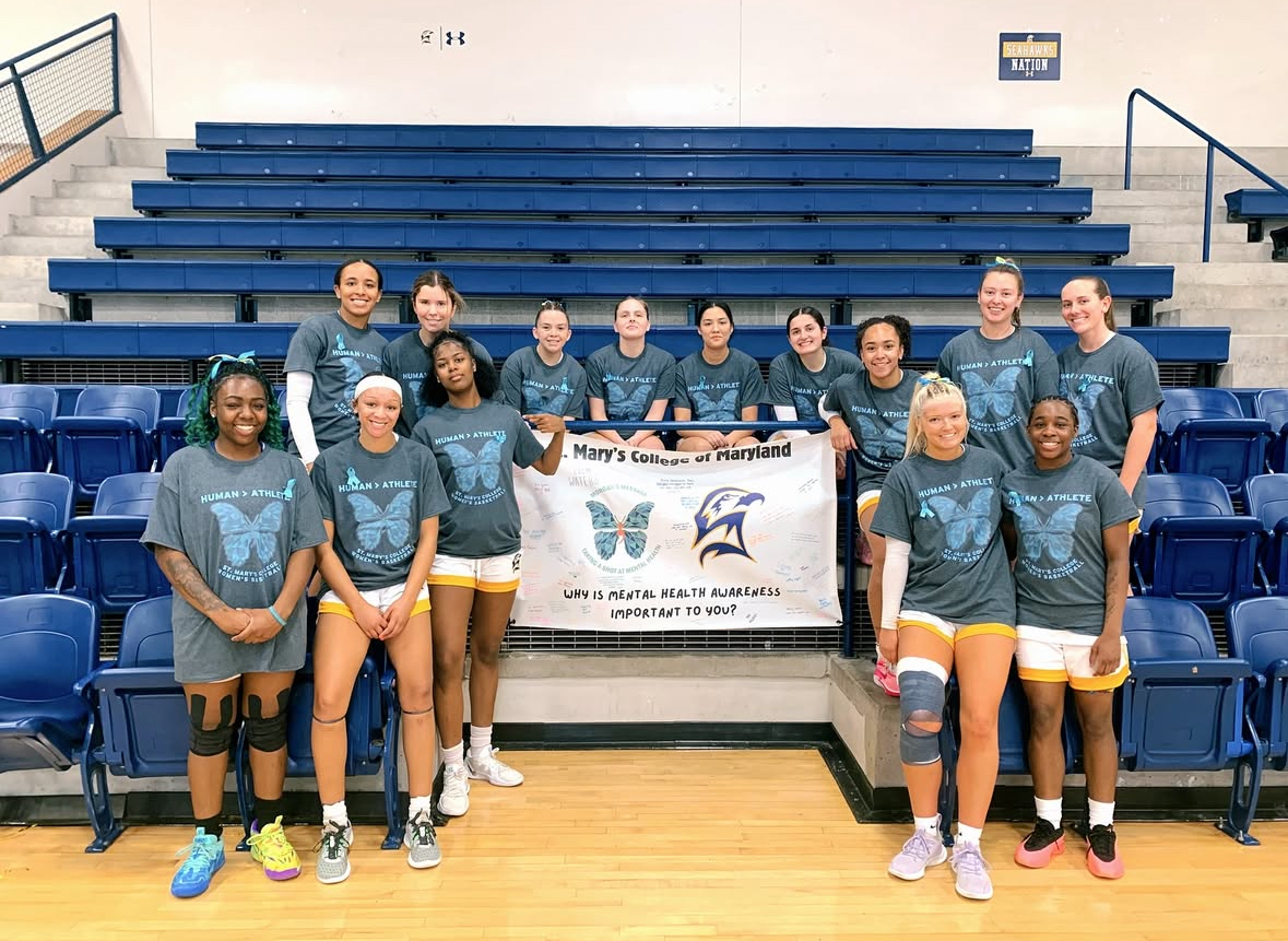 A women's volleyball team poses in a gym, holding a sign promoting mental health awareness from St. Mary's College of Maryland.