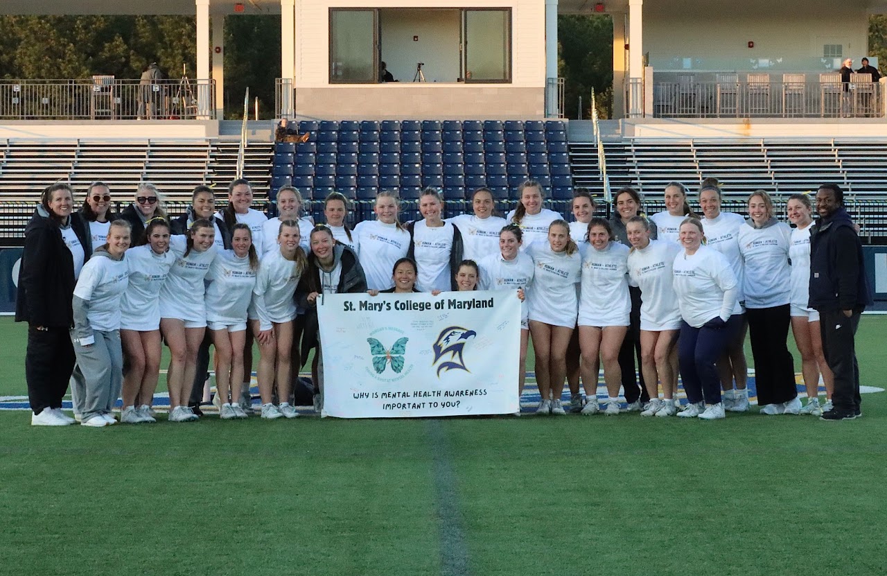 A women's sports team poses on a field holding a St. Mary's College of Maryland banner promoting mental health awareness.