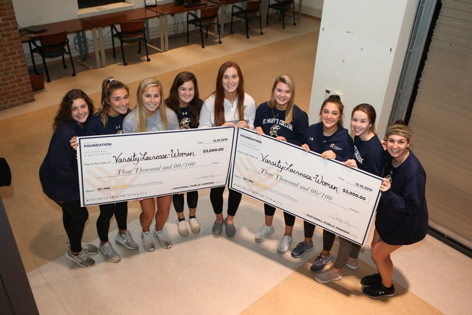 Varsity Women's Lacrosse team holding winning checks Varsity Women's Lacrosse team holding winning checks