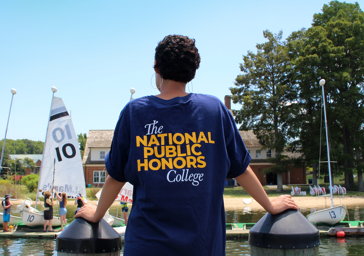 student facing riverfront with national public honors college tee shirt