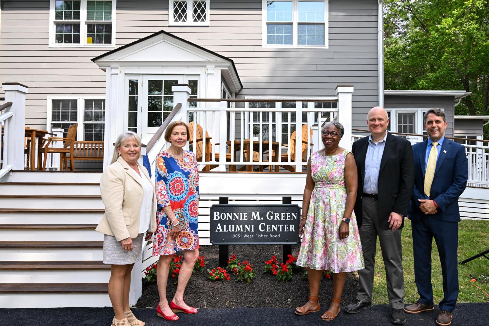Five people stand in front of the Bonnie M. Green Alumni Center, posing for a photo near the building's entrance and a sign with the center's name.