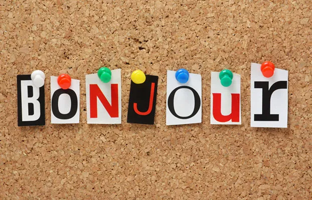The word "Bonjour" is spelled out using cut-out letters from magazines, each pinned with colorful pushpins to a corkboard.