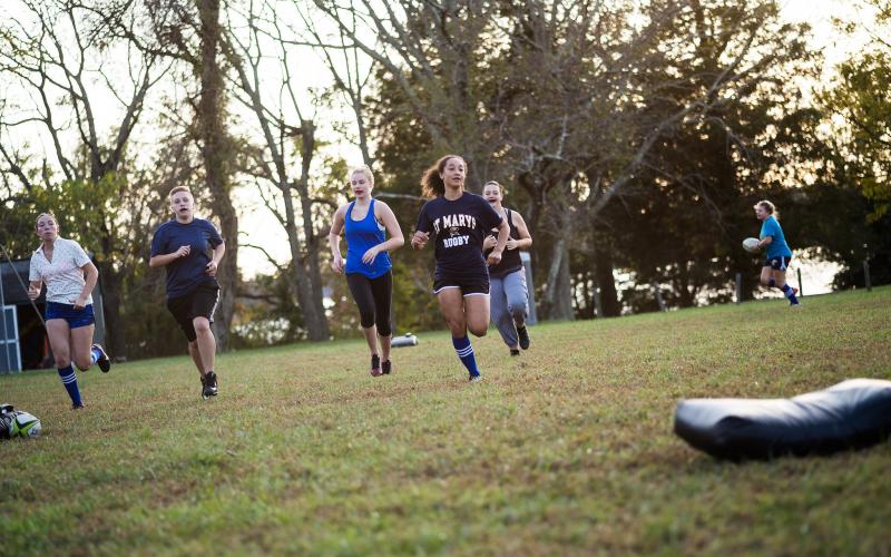 Several Students running on a field with a rugby ball