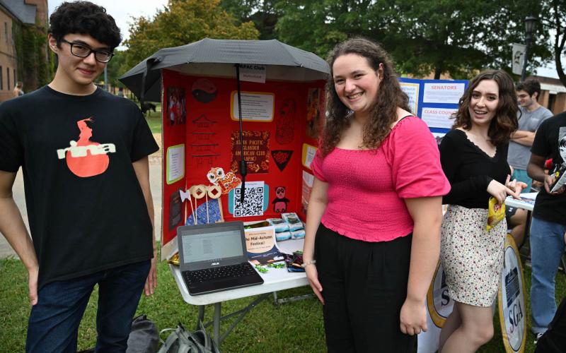 Three students posing in front of an Asian Pacific Islander American Culture (APAC) Club table